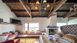 Una sala de estar moderna con techo alto, chimenea, sofá, sillón rojo y vistas a las montañas.