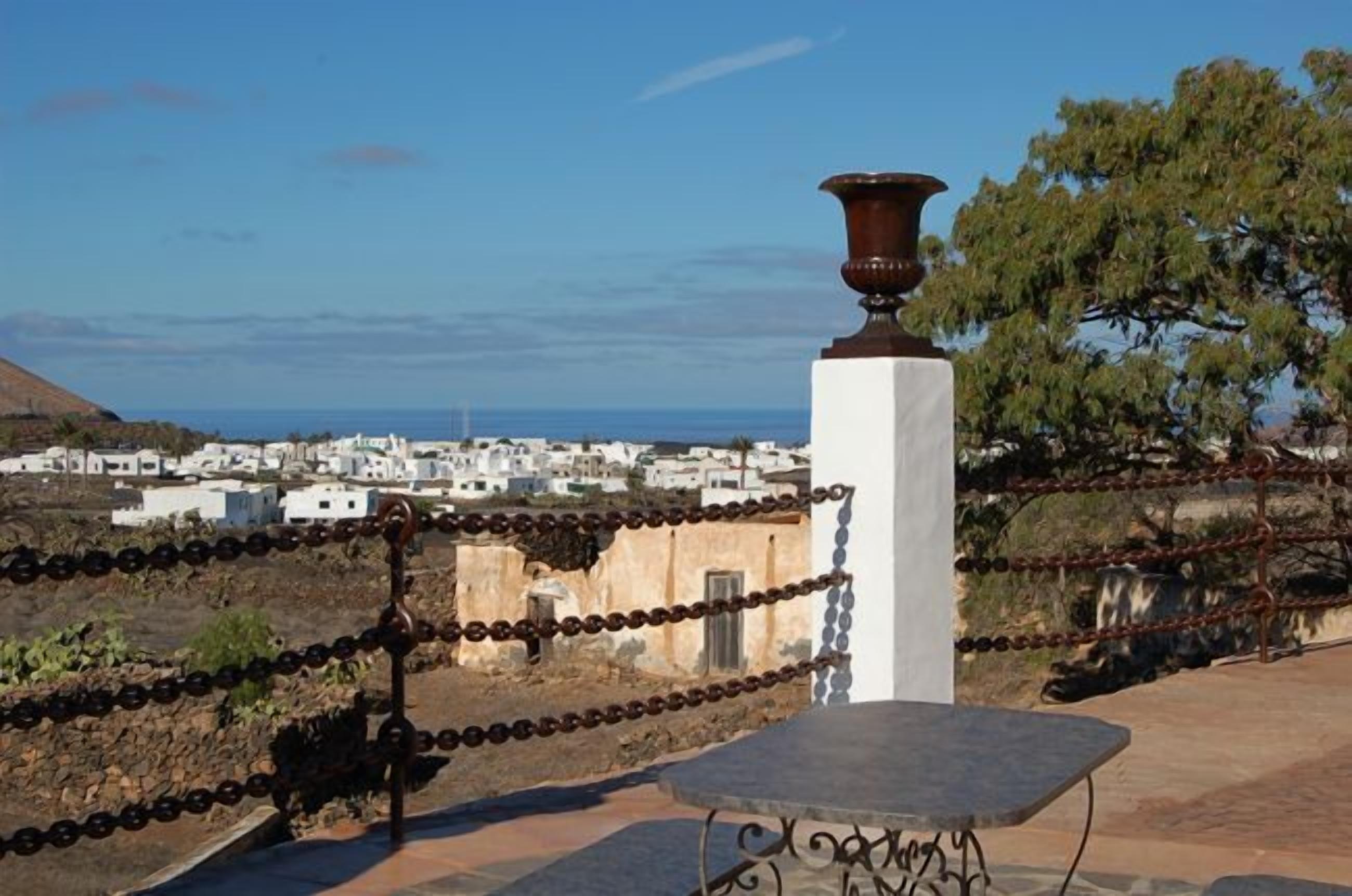 Vista costera con un edificio blanco, una cerca de metal y una mesa de piedra.