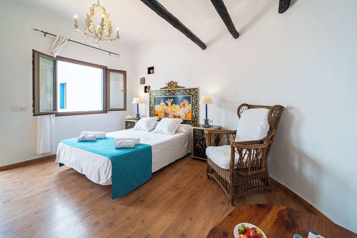 Quarto com cama, uma cadeira, uma mesa e um quadro.