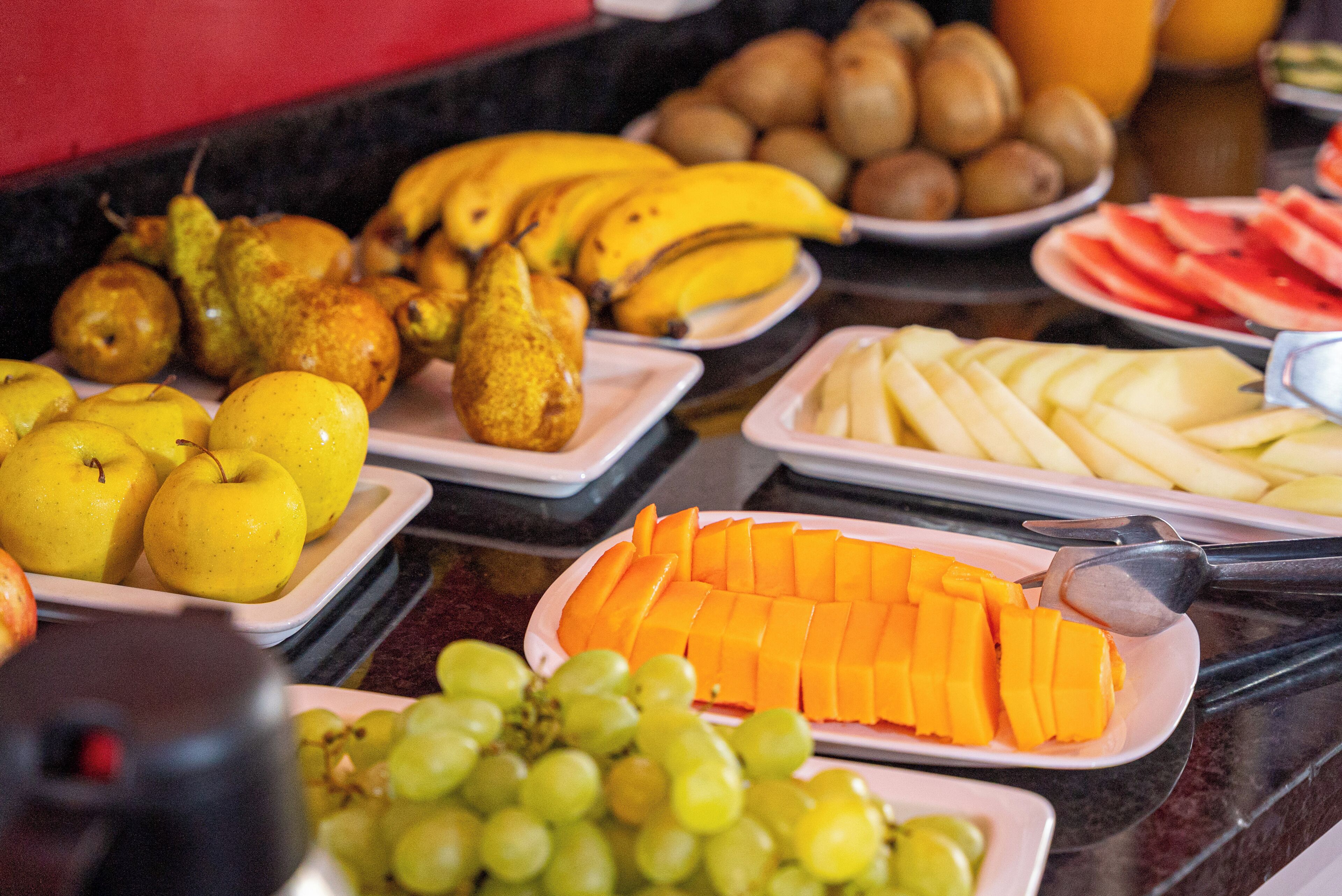 Ein reichhaltiges Buffet mit verschiedenen Früchten und Gemüse, darunter Äpfel, Birnen, Bananen, Kiwis, Wassermelone und Trauben.