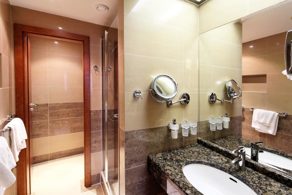 A modern bathroom with a glass-enclosed shower, a granite countertop, and a large mirror.