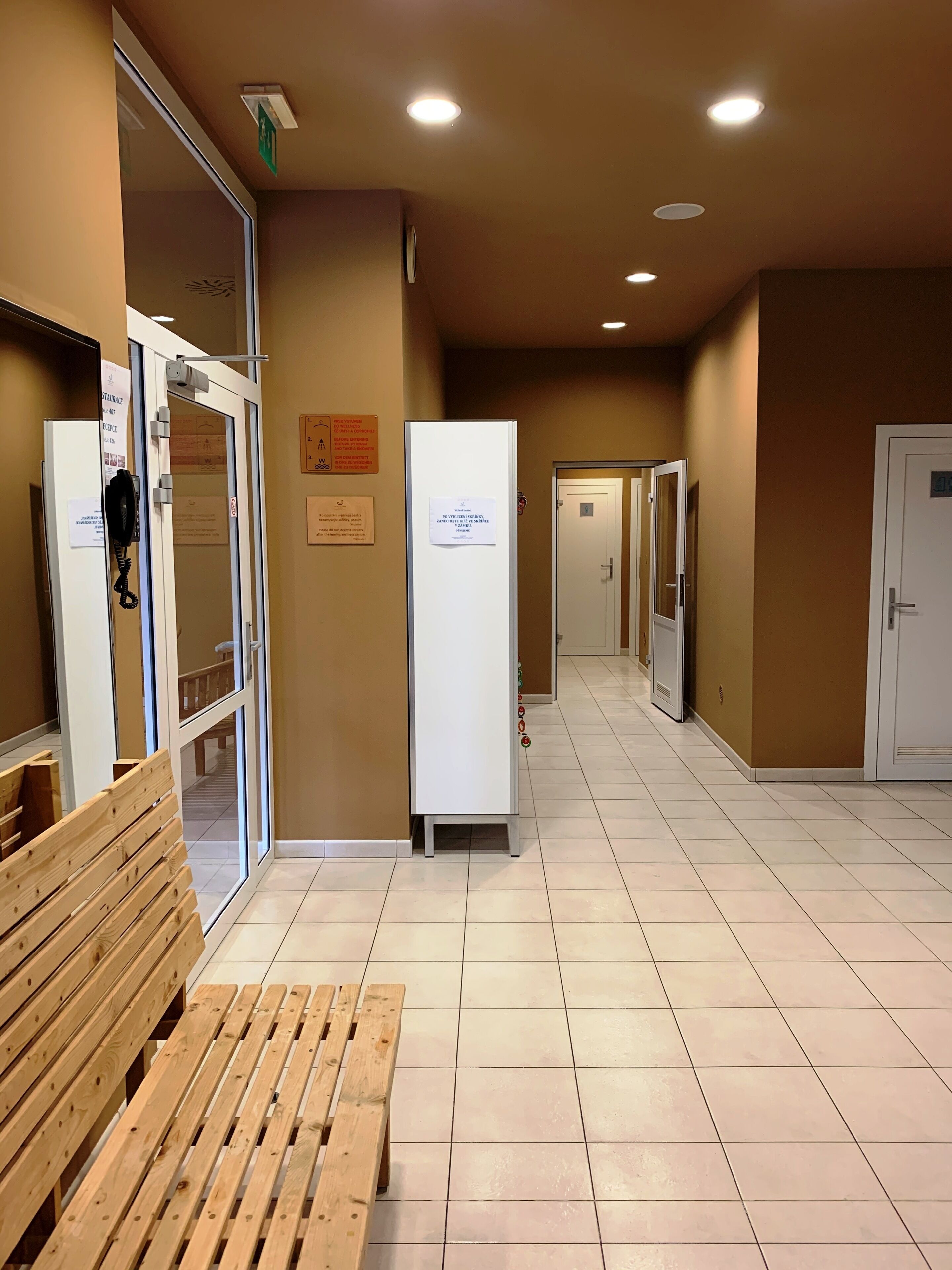 A corridor with a wooden bench, a refrigerator, and a door with a sign.