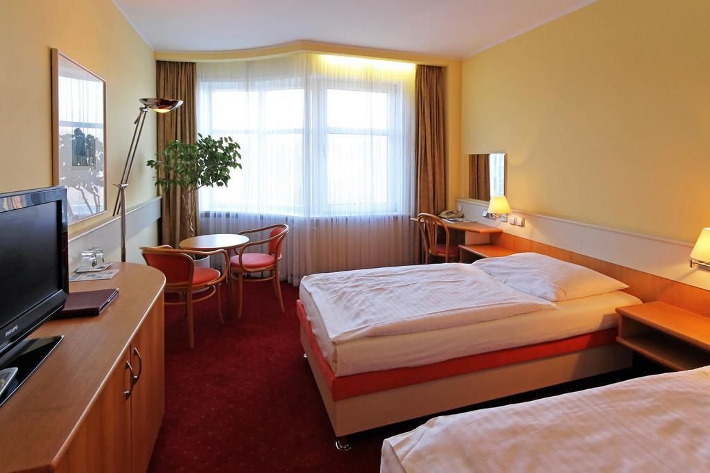 Une chambre d’hôtel avec un lit, un bureau, une chaise, une télévision et une fenêtre avec des rideaux.