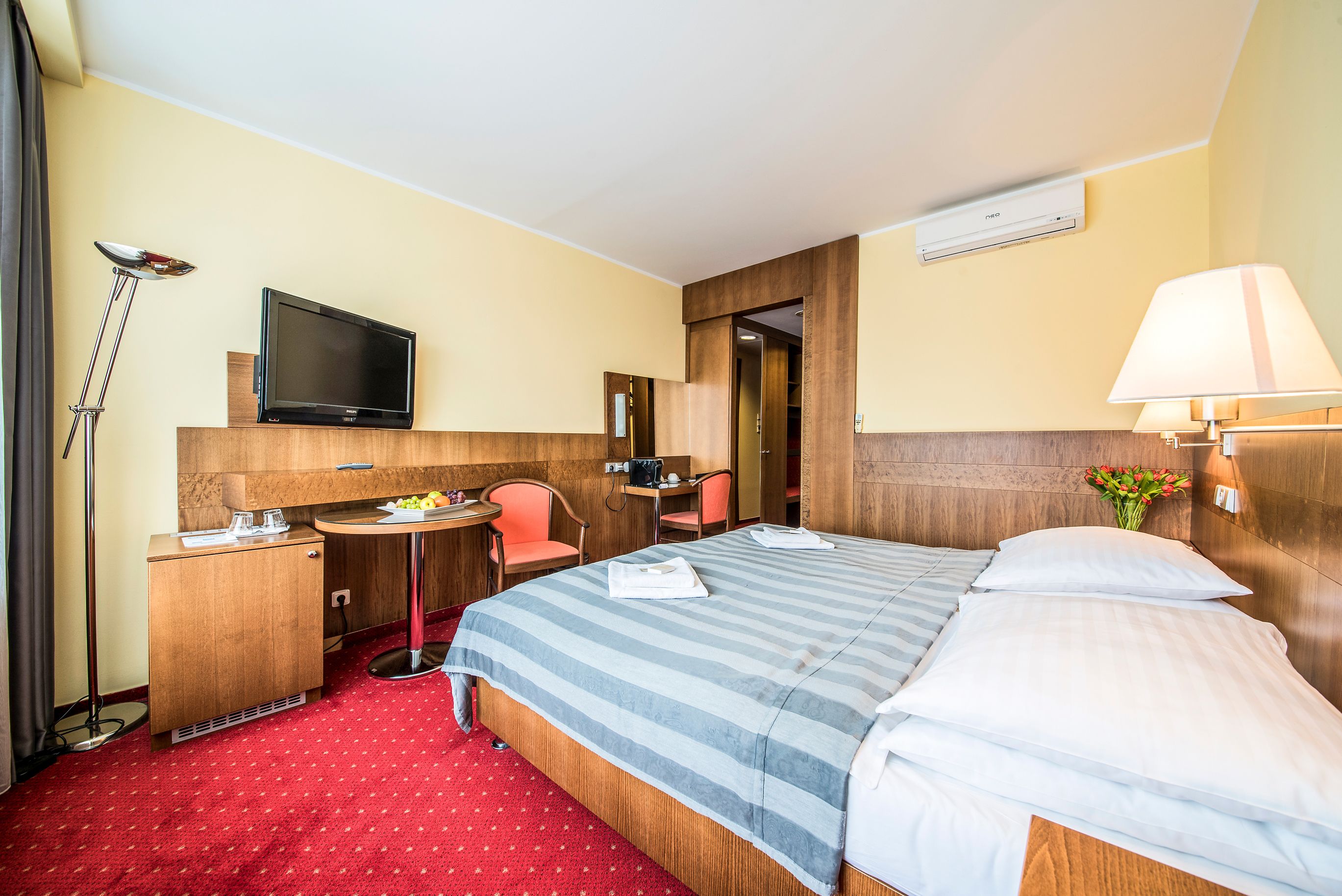 A hotel room with a bed, a desk, a chair, a TV, and a lamp.