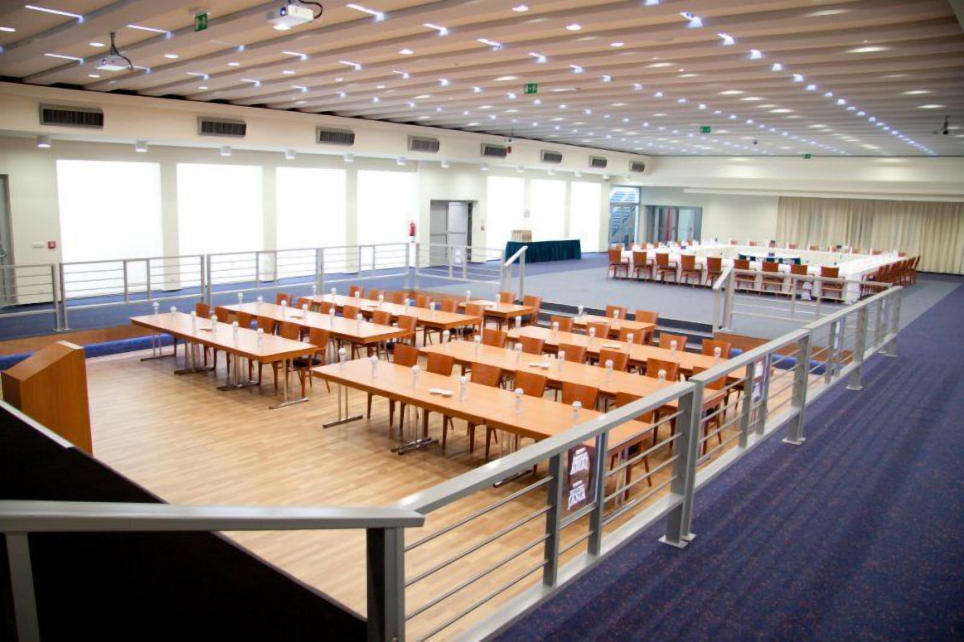 A large conference room with multiple tables and chairs, a stage, and a balcony with a railing.