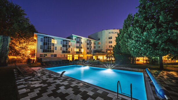 A hotel with a swimming pool, outdoor seating, and a well-lit facade. - Hotel Jana (Prerov)