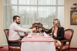 A dining table with a pink tablecloth, two chairs, and a vase with a plant. - Hotel Jana (Prerov)