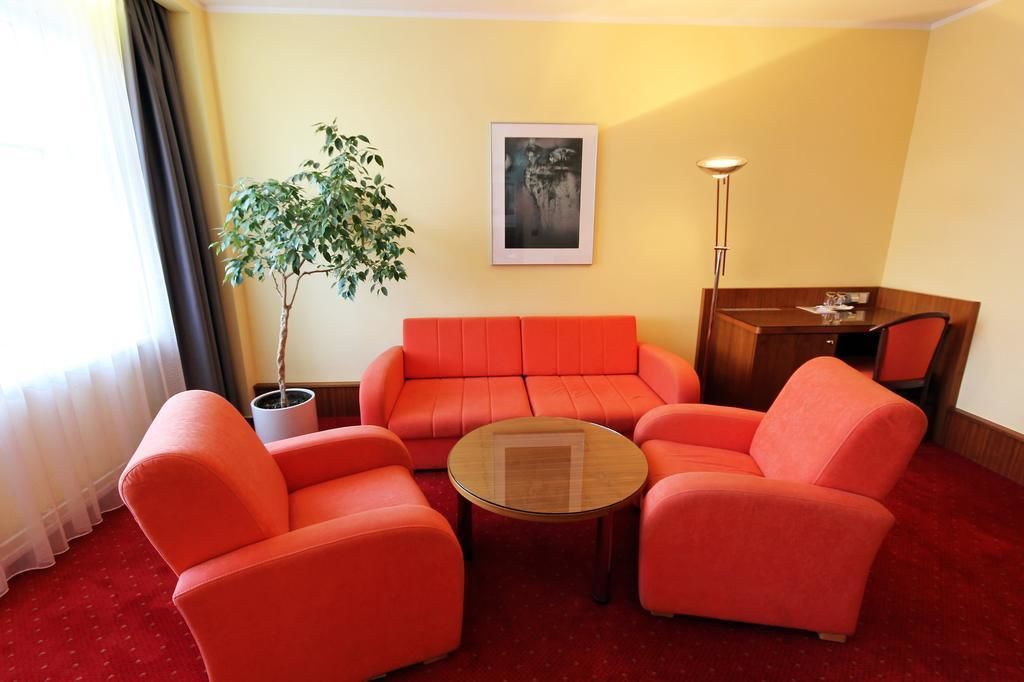 Una habitación con un sofá rojo, una mesa de centro redonda, una planta en maceta, un cuadro en la pared y un escritorio con una lámpara.