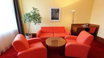 Una habitación con un sofá rojo, una mesa de centro redonda, una planta en maceta, un cuadro en la pared y un escritorio con una lámpara.