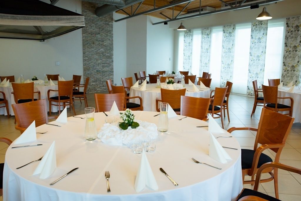 A dining area with round tables, each set with white tablecloths, chairs, and centerpieces.