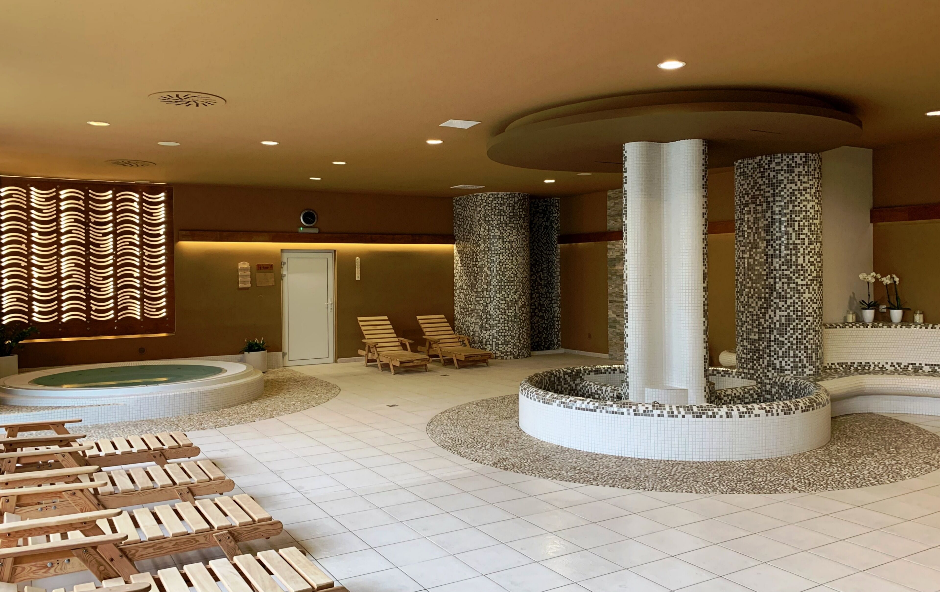 A spa area with a hot tub, wooden loungers, and mosaic pillars.