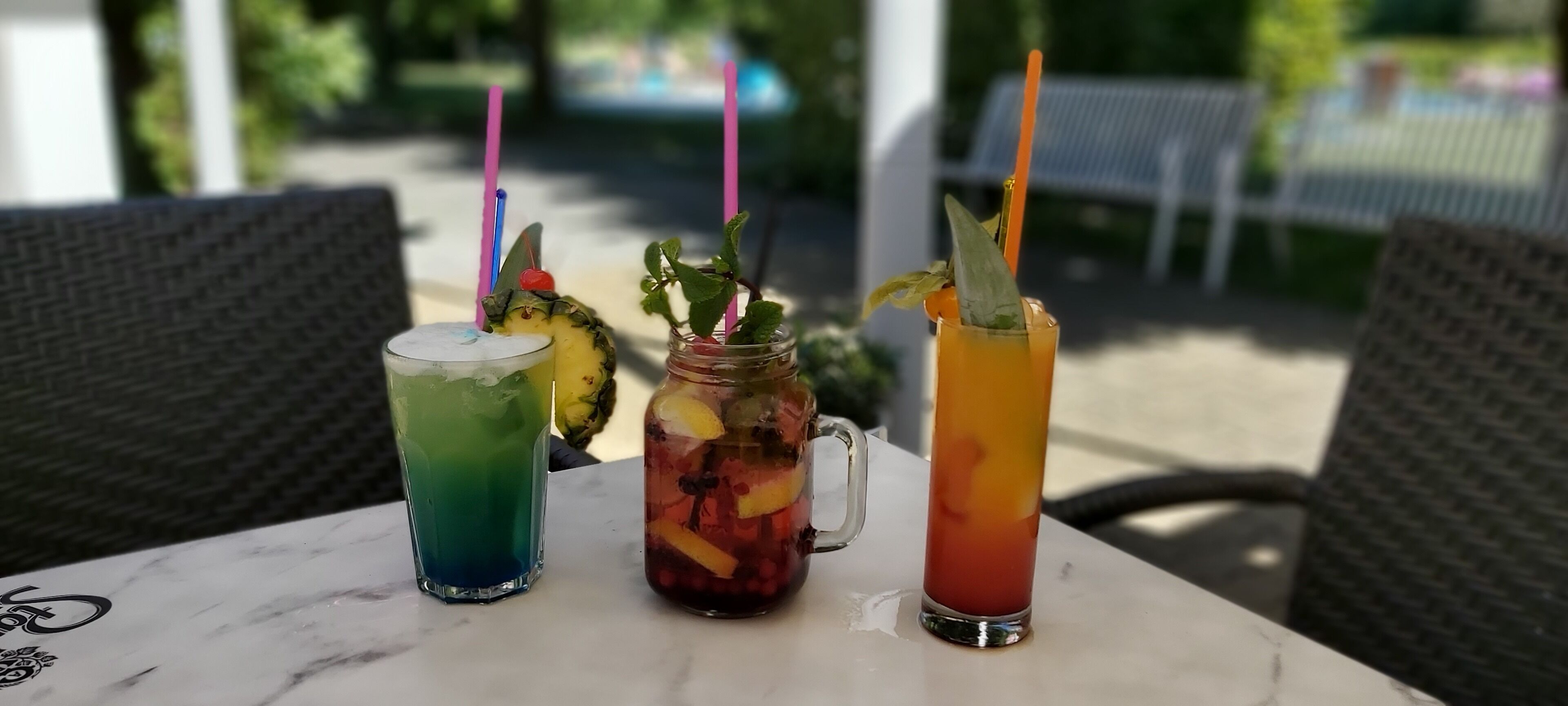 Three drinks on a table with wicker chairs around.