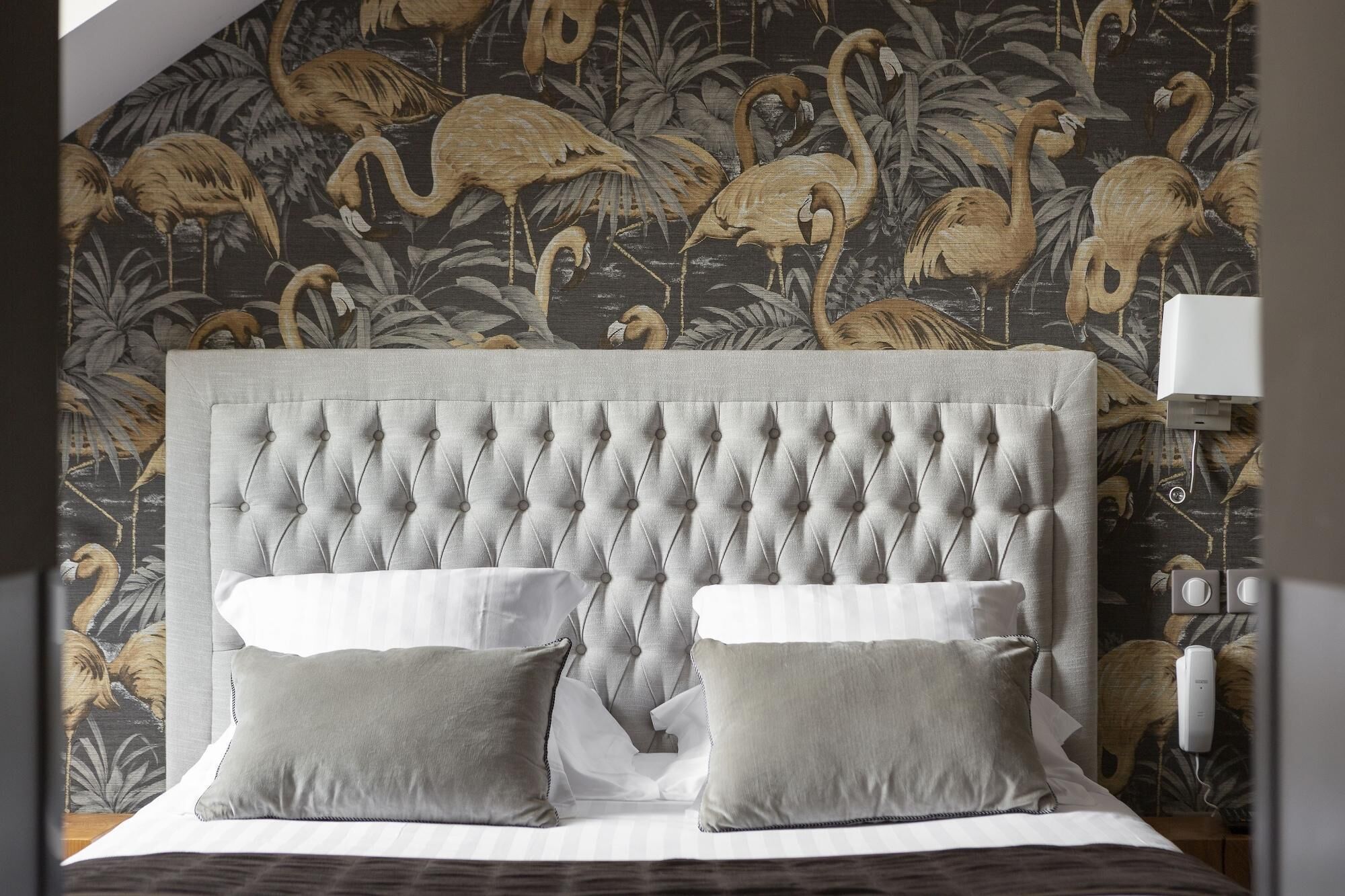 A bed with a tufted headboard, two pillows, and a floral wallpaper background.