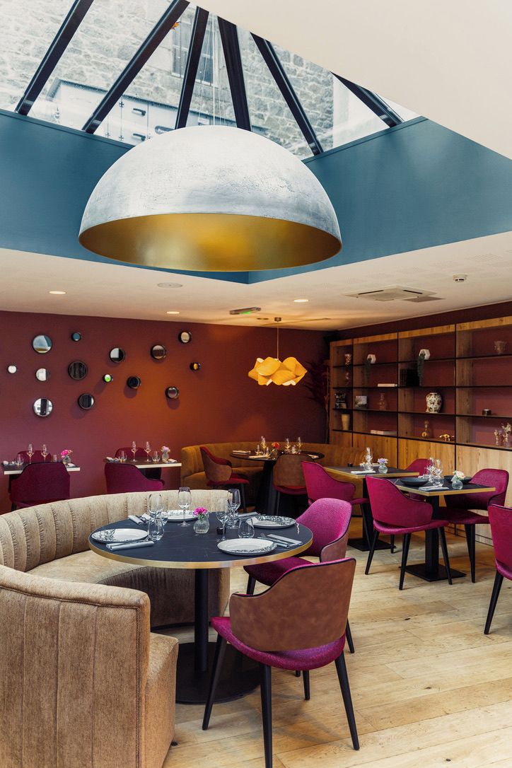 A modern restaurant with round tables, purple chairs, and a unique ceiling design.