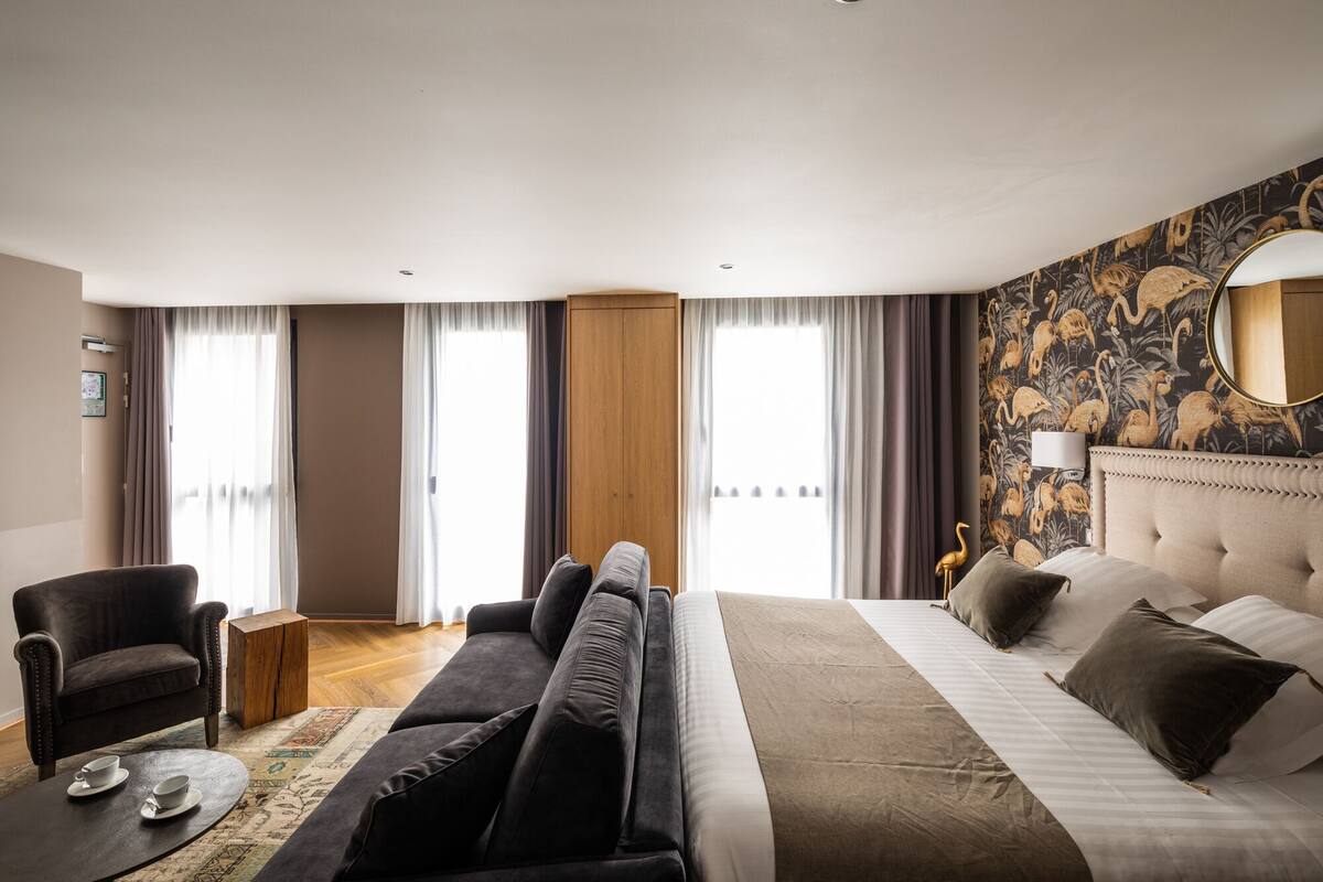 A hotel room with a large bed, a sofa, a chair, and a small table with cups.