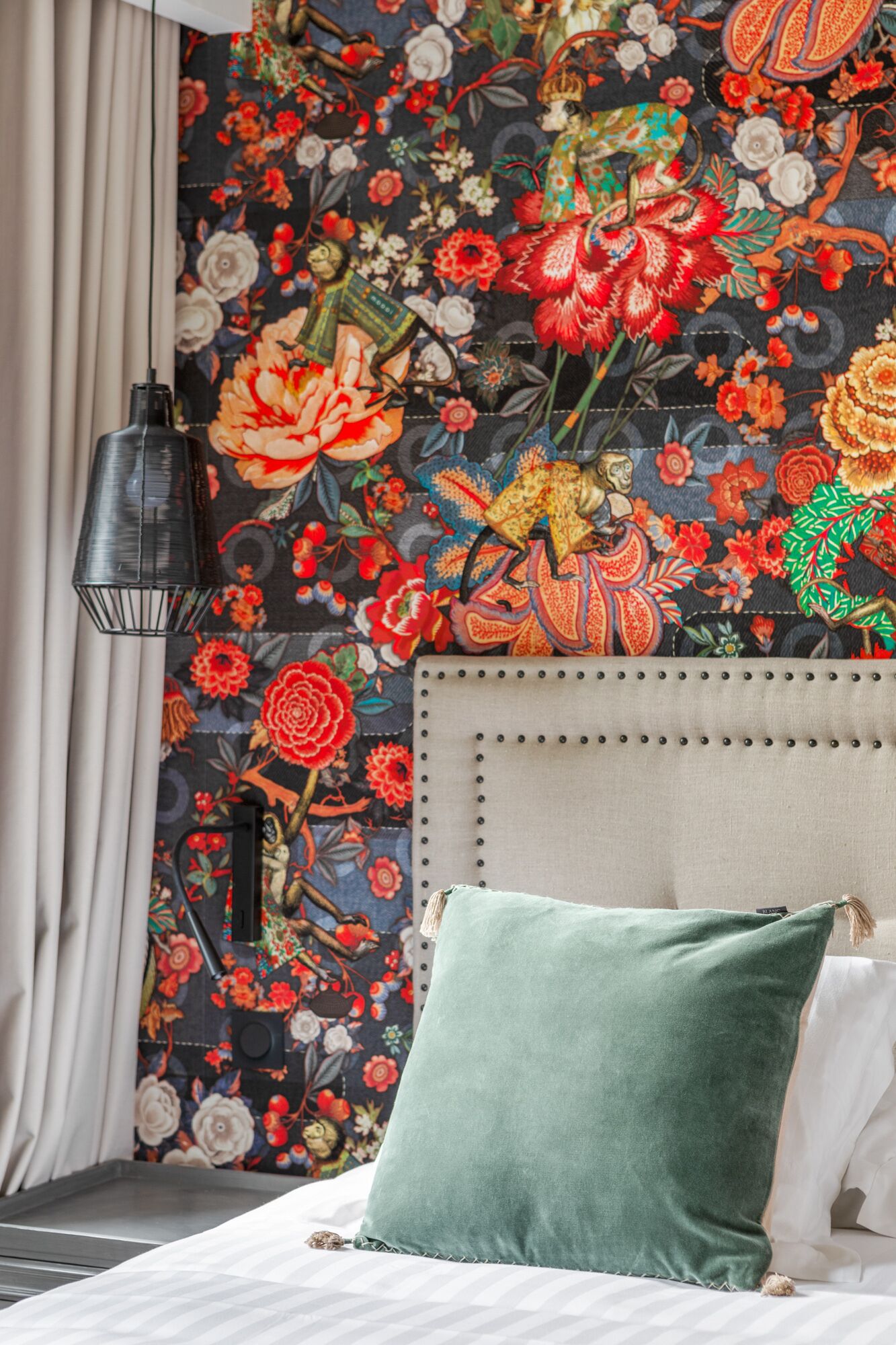 A bedroom with a floral-patterned wall, a grey headboard, and a green pillow.