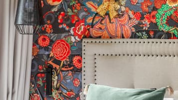 A bedroom with a floral-patterned wall, a grey headboard, and a green pillow.