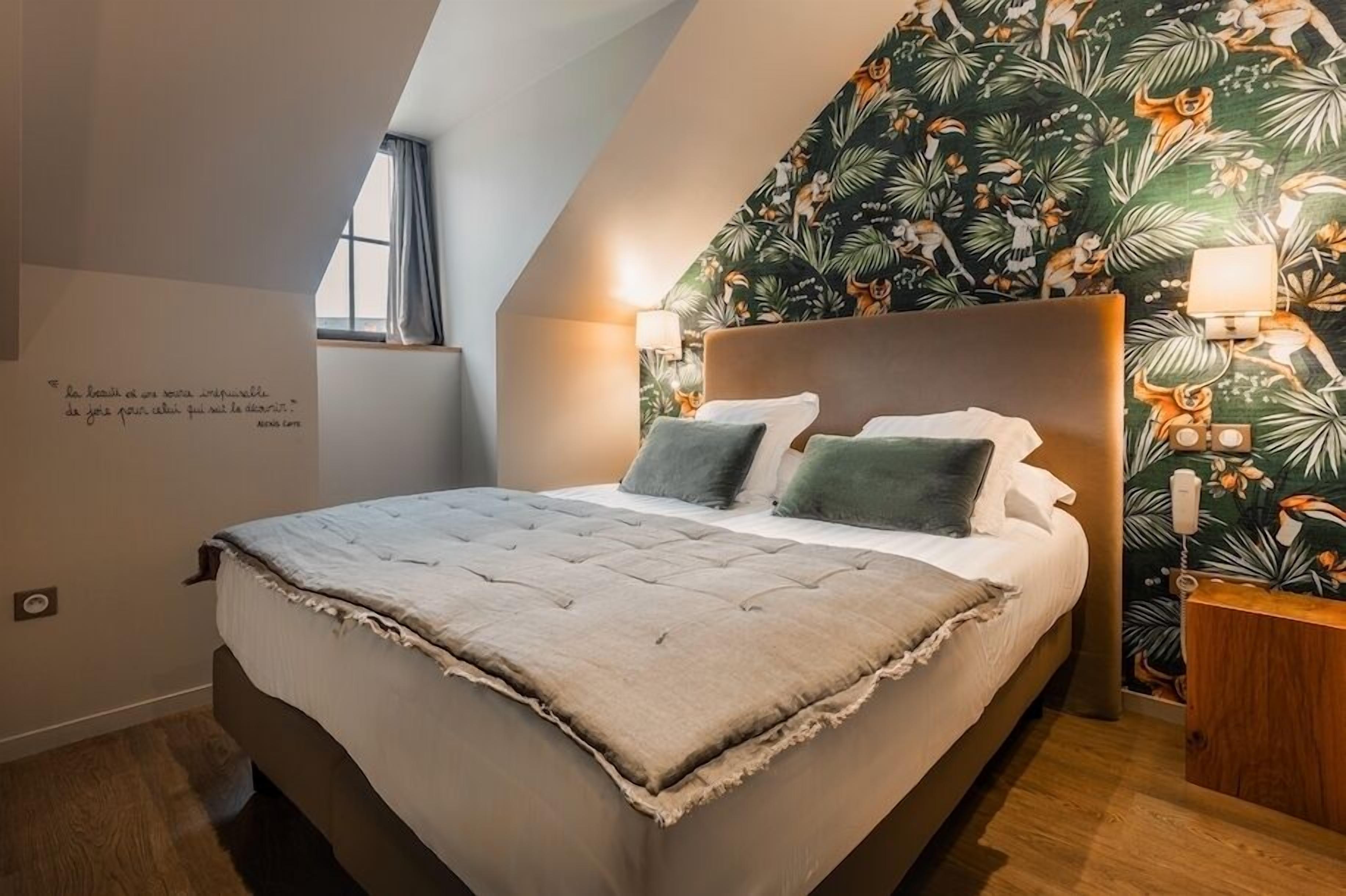 A bedroom with a large bed, a wall with tropical wallpaper, and a quote on the wall.