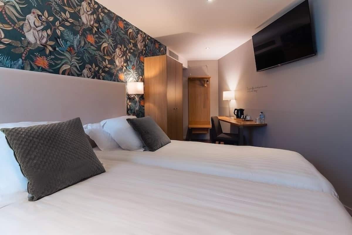 A hotel room with a large bed, a desk, a chair, a TV, and a wall with a floral pattern.