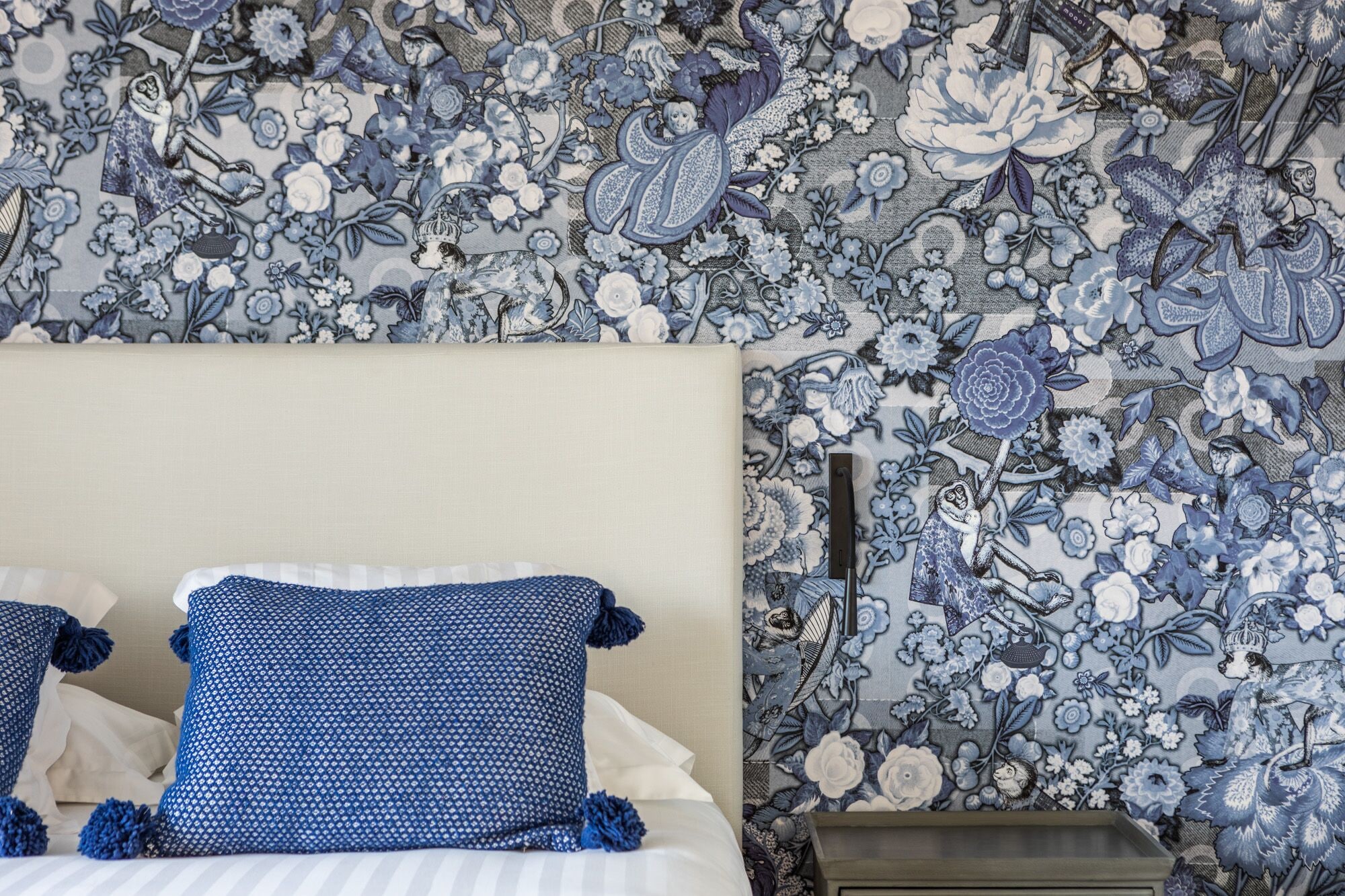 Een slaapkamer met bloemenbehang, een bed met blauwe kussens en een nachtkastje.