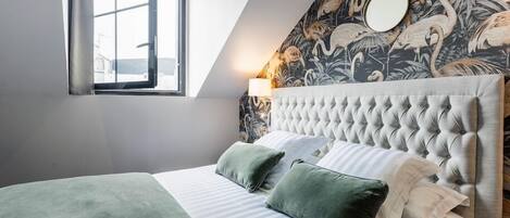 Un dormitorio con cabecera capitonada, un ventanal grande y una pared con papel tapiz tropical.