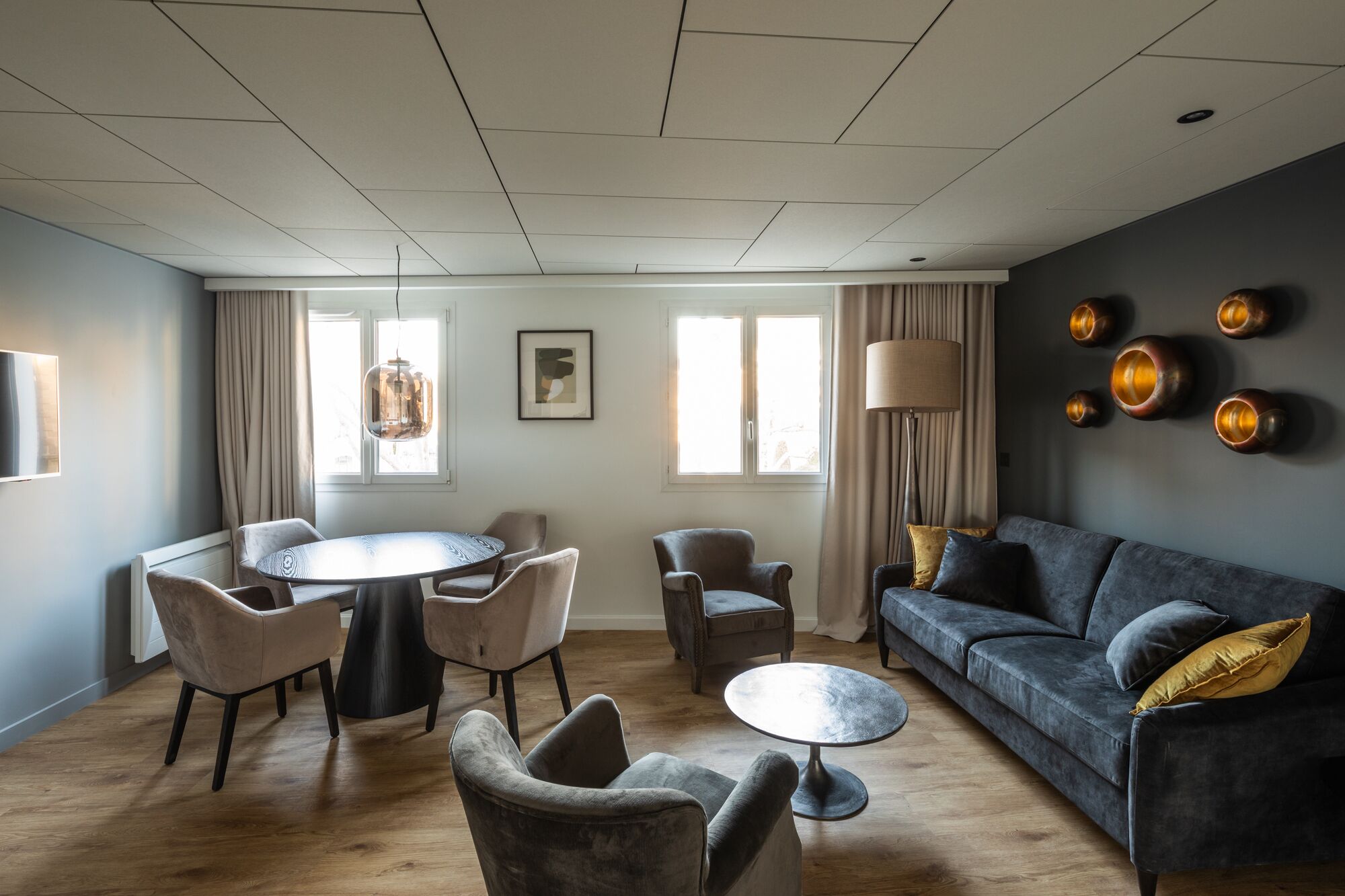 Una sala de estar moderna con un sofá gris, una mesa de centro redonda y un comedor con una mesa y sillas redondas.
