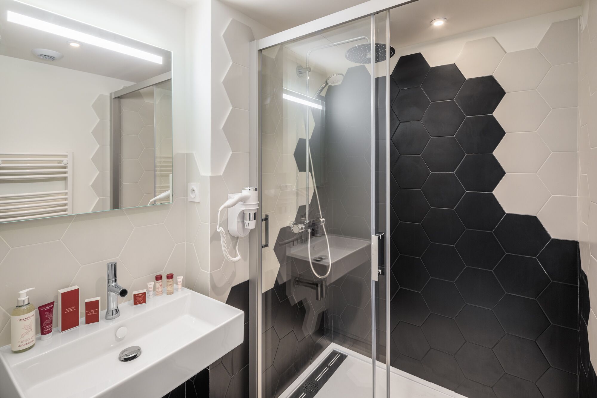 Un baño moderno con ducha de vidrio, lavamanos blanco y artículos de aseo, y un espejo.