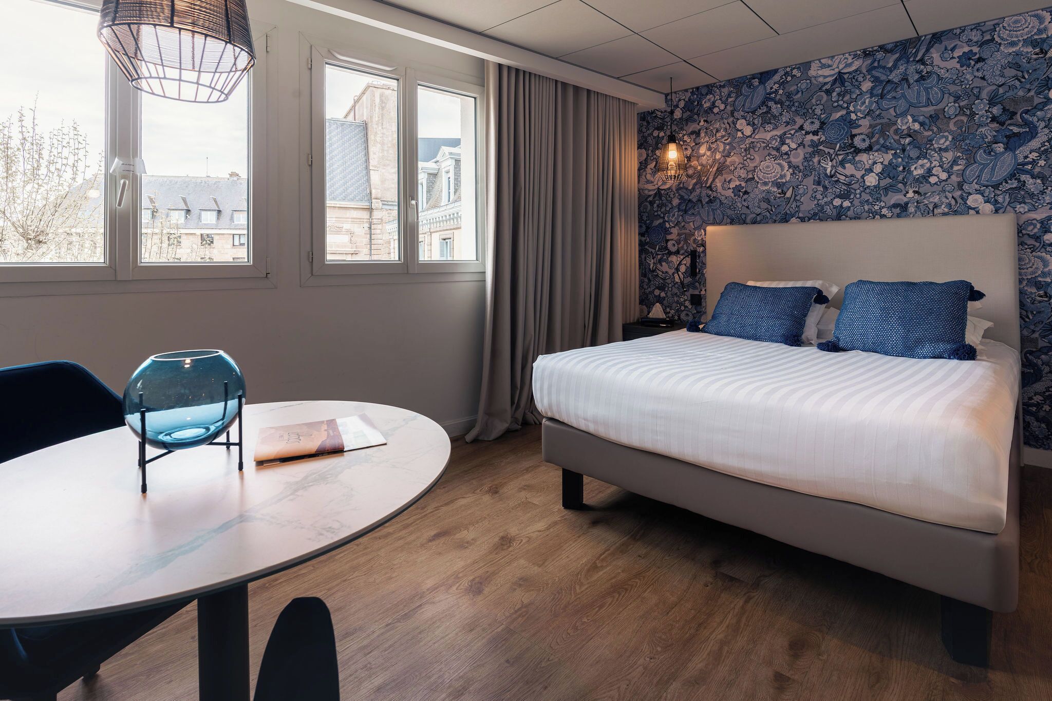 Un dormitorio con una cama, una mesa redonda con una silla y una ventana con cortinas.