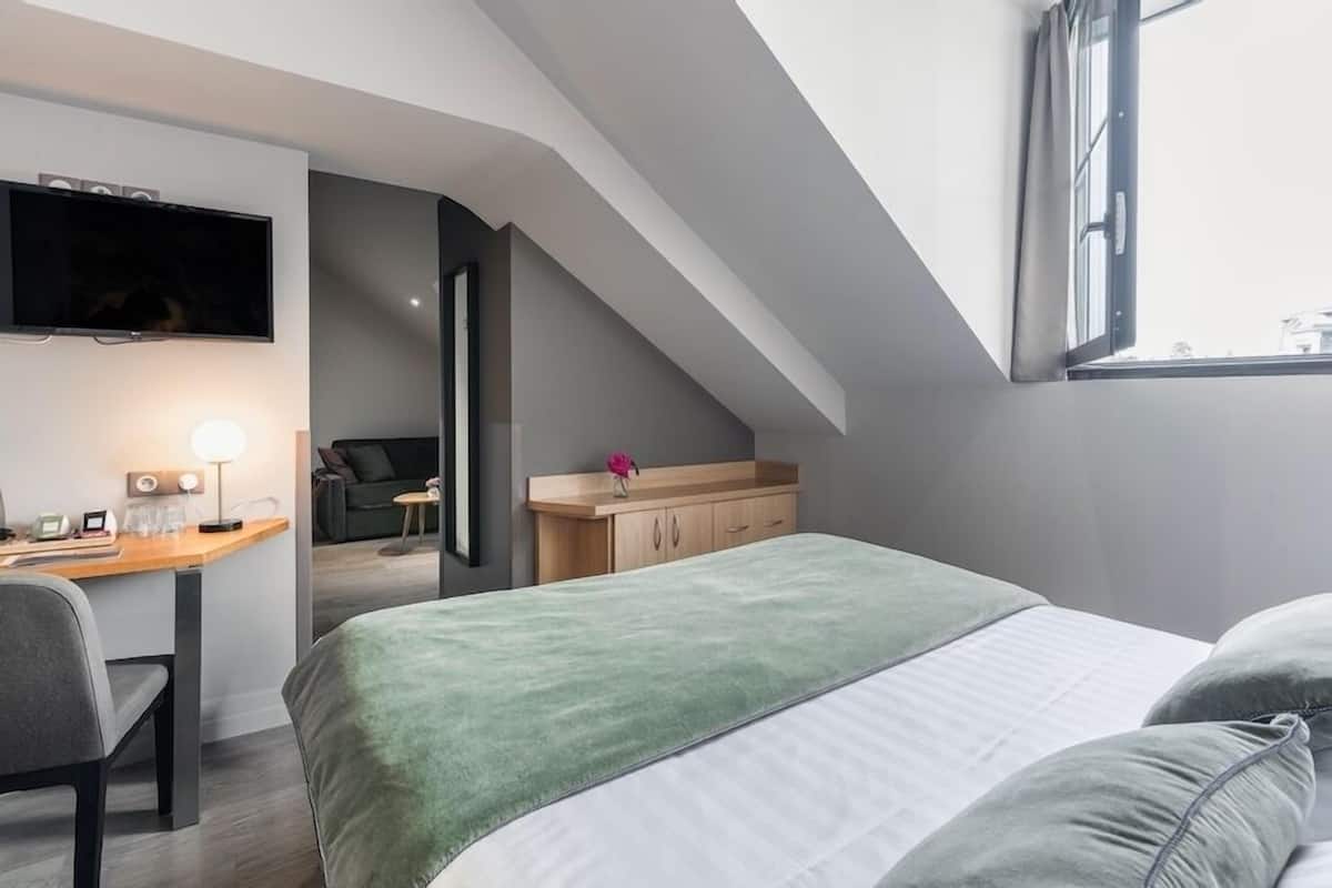 A modern, compact bedroom with a bed, a desk, a chair, and a TV mounted on the wall.