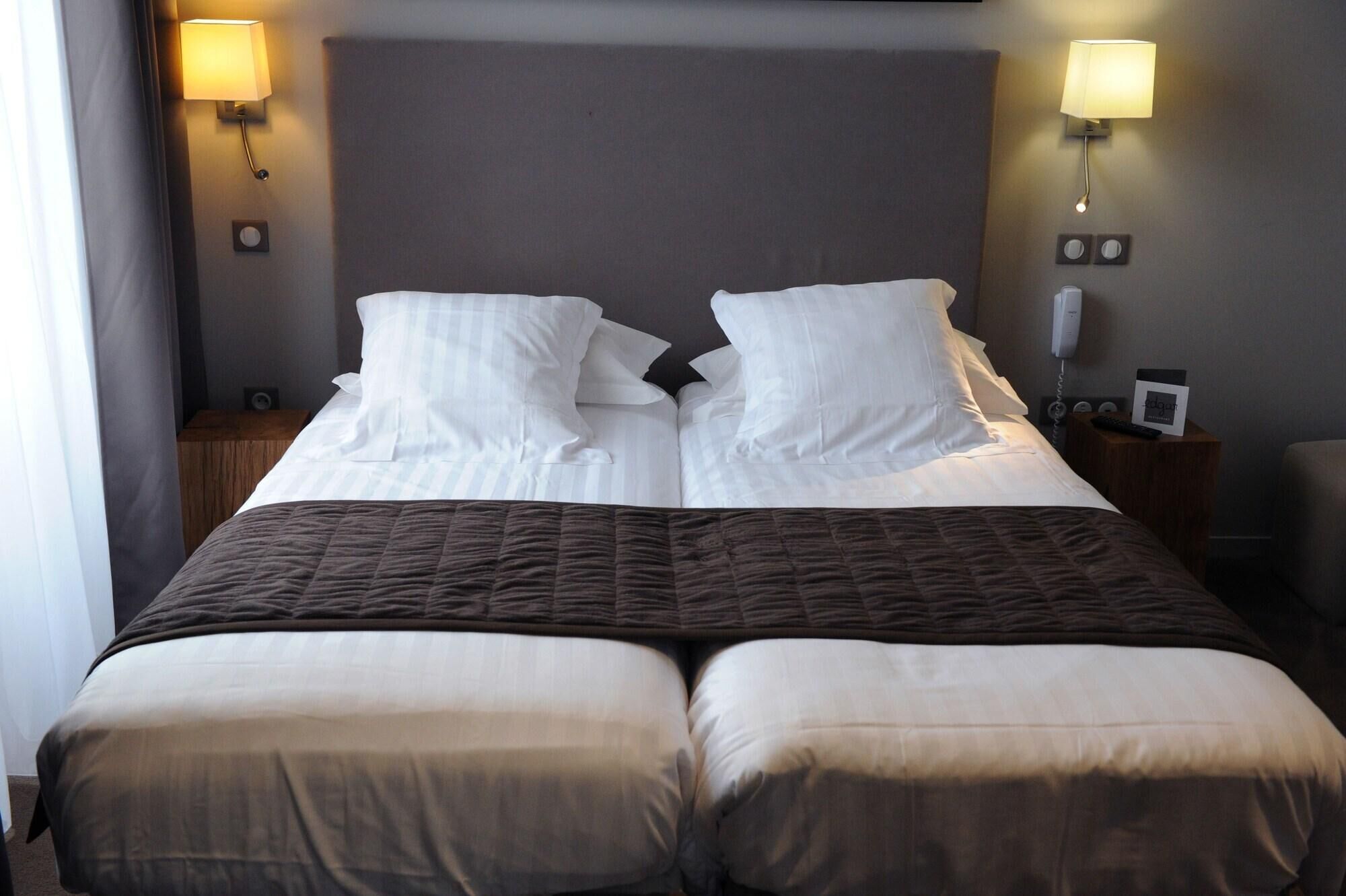 A double bed with two pillows, a dark brown quilt, a bedside table with a lamp, and a phone.