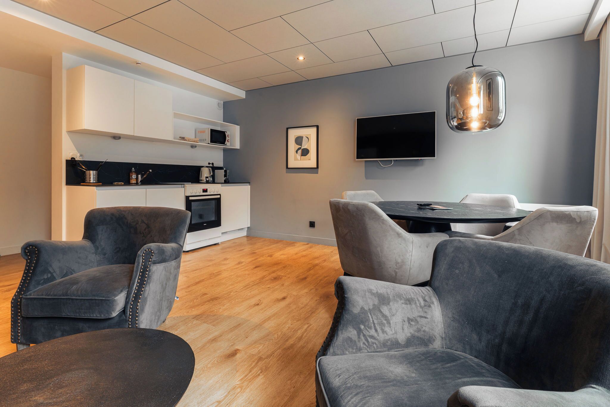 Un salon moderne comprenant un coin repas, une cuisine avec des meubles blancs et un téléviseur à écran plat.