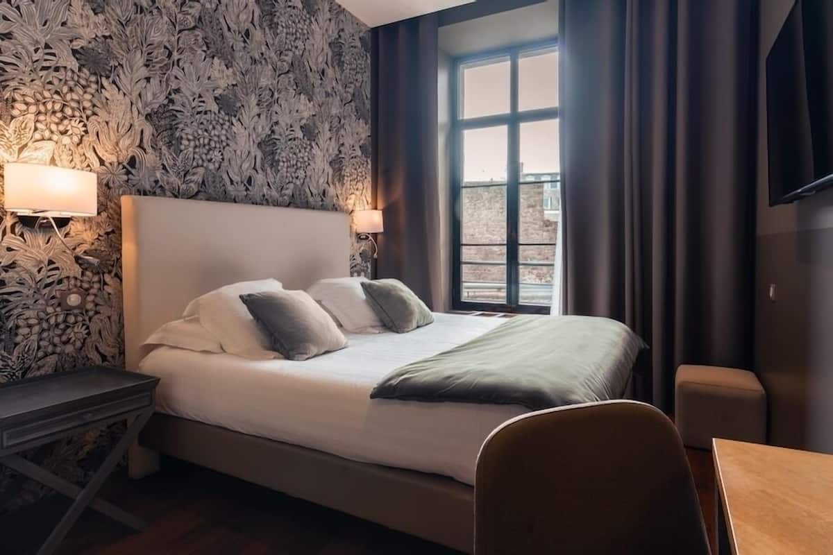 A hotel room with a bed, bedside lamps, a window with curtains, a TV, and a small table.