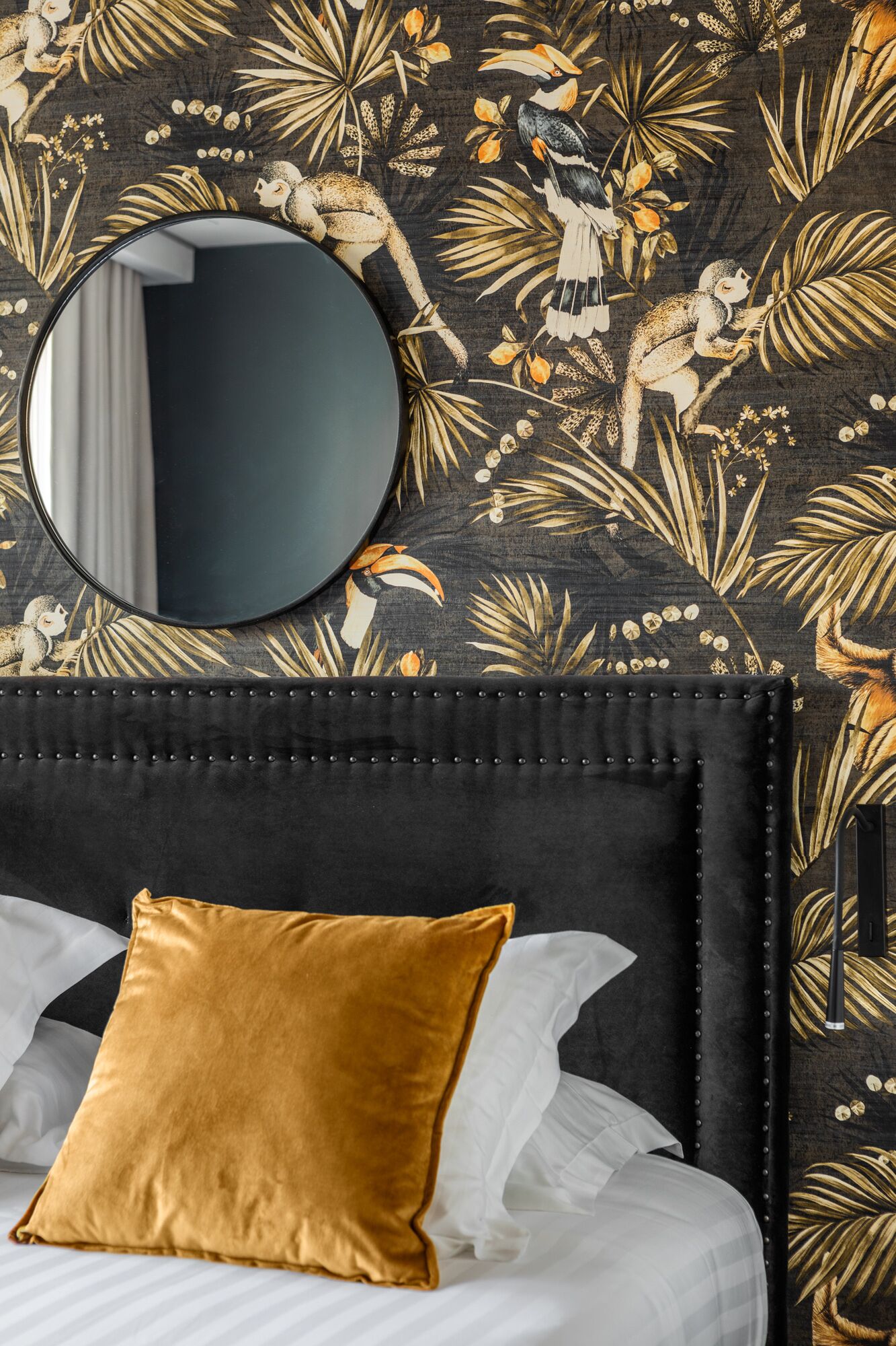 A bed with a black upholstered headboard, a round mirror, and a gold pillow.