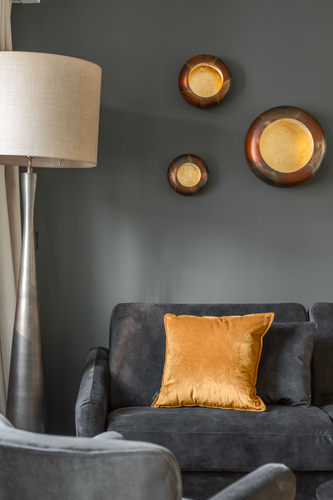 Un salon moderne avec un canapé gris foncé, un coussin jaune moutarde et une lampe sur pied.