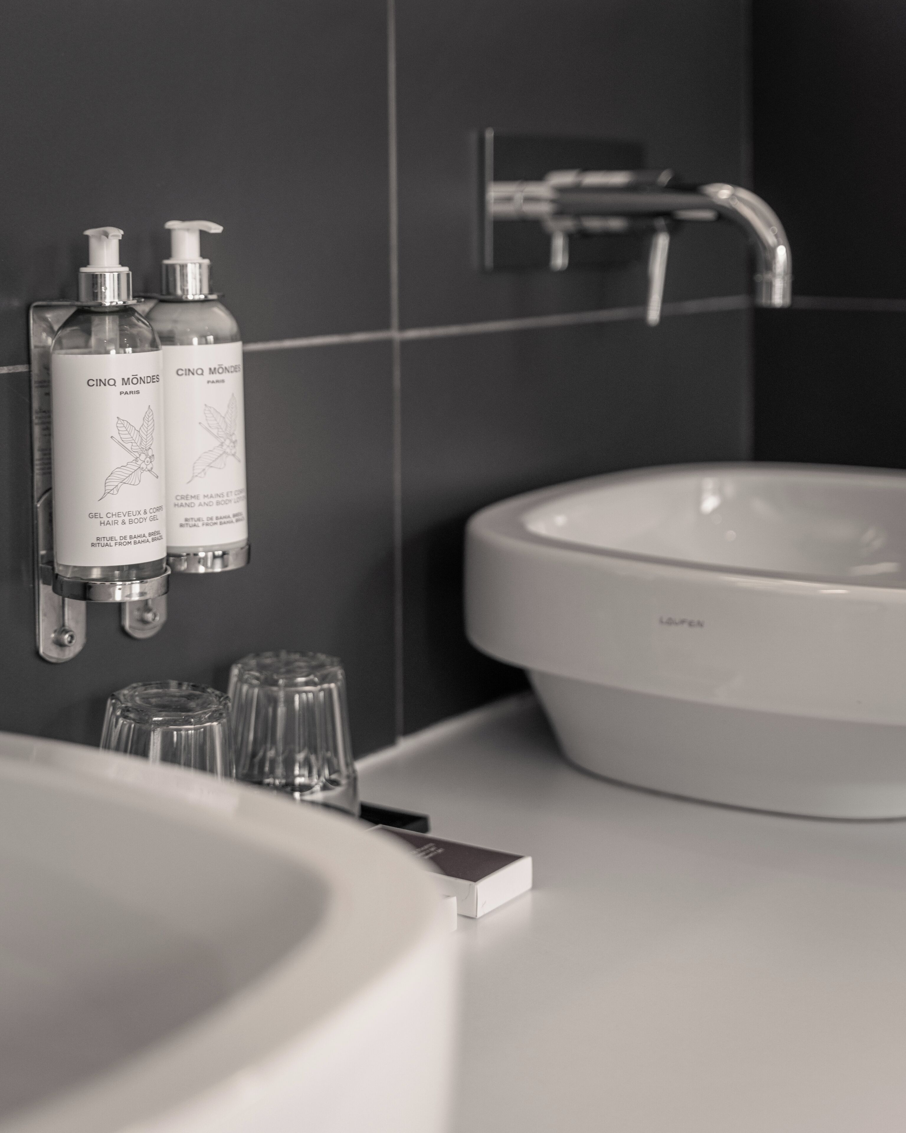 A bathroom with a white sink, two bottles of Cinq Mondes Paris hair and body care, and a modern faucet.