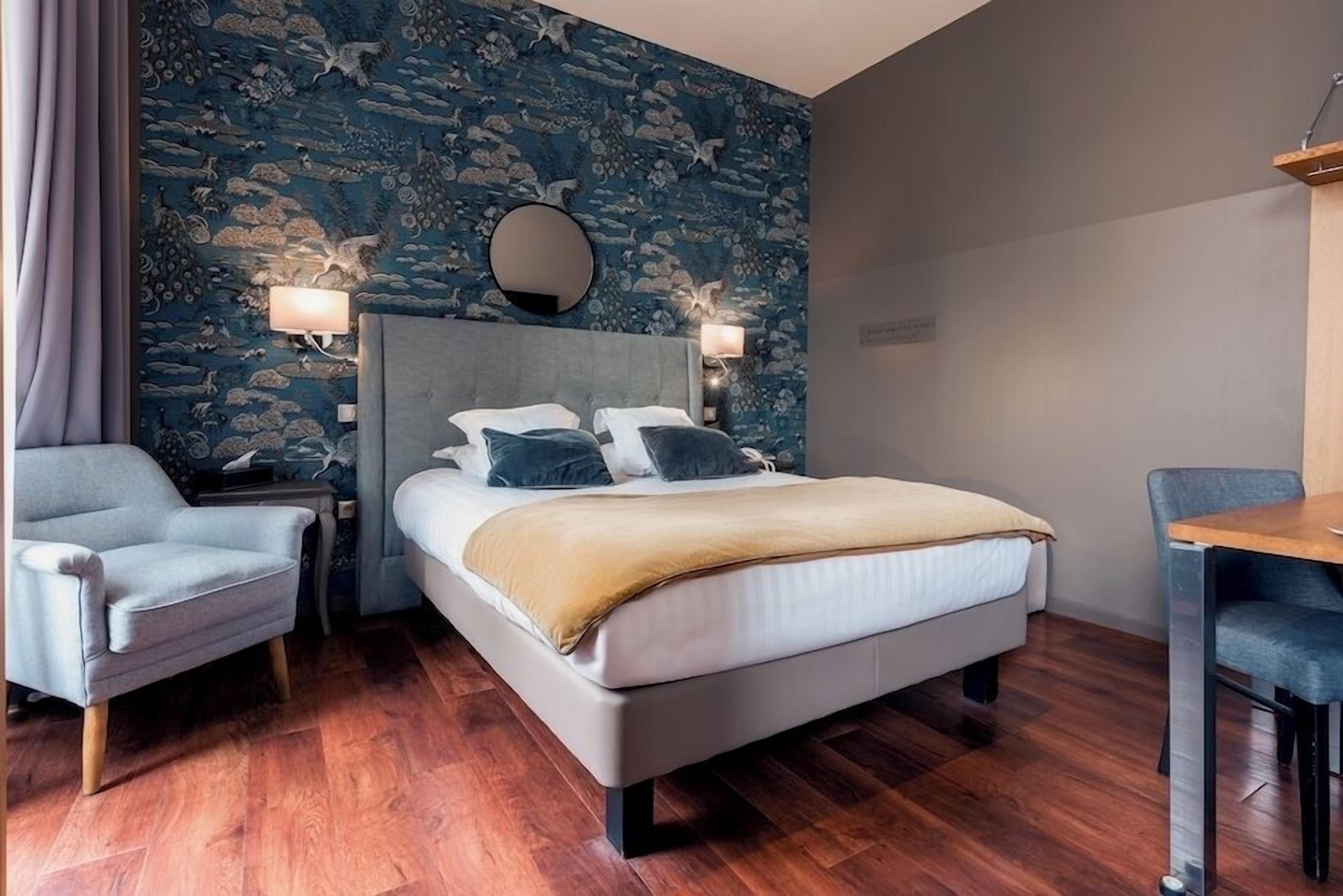 Una habitación de hotel con una cama, una silla, un escritorio y una pared con un estampado floral azul.