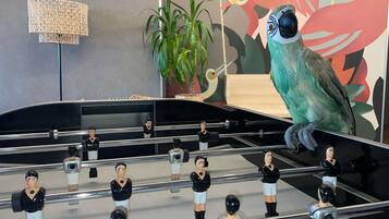 Una mesa de fútbol de mesa con figuras, una lámpara y una pared con un mural tropical.