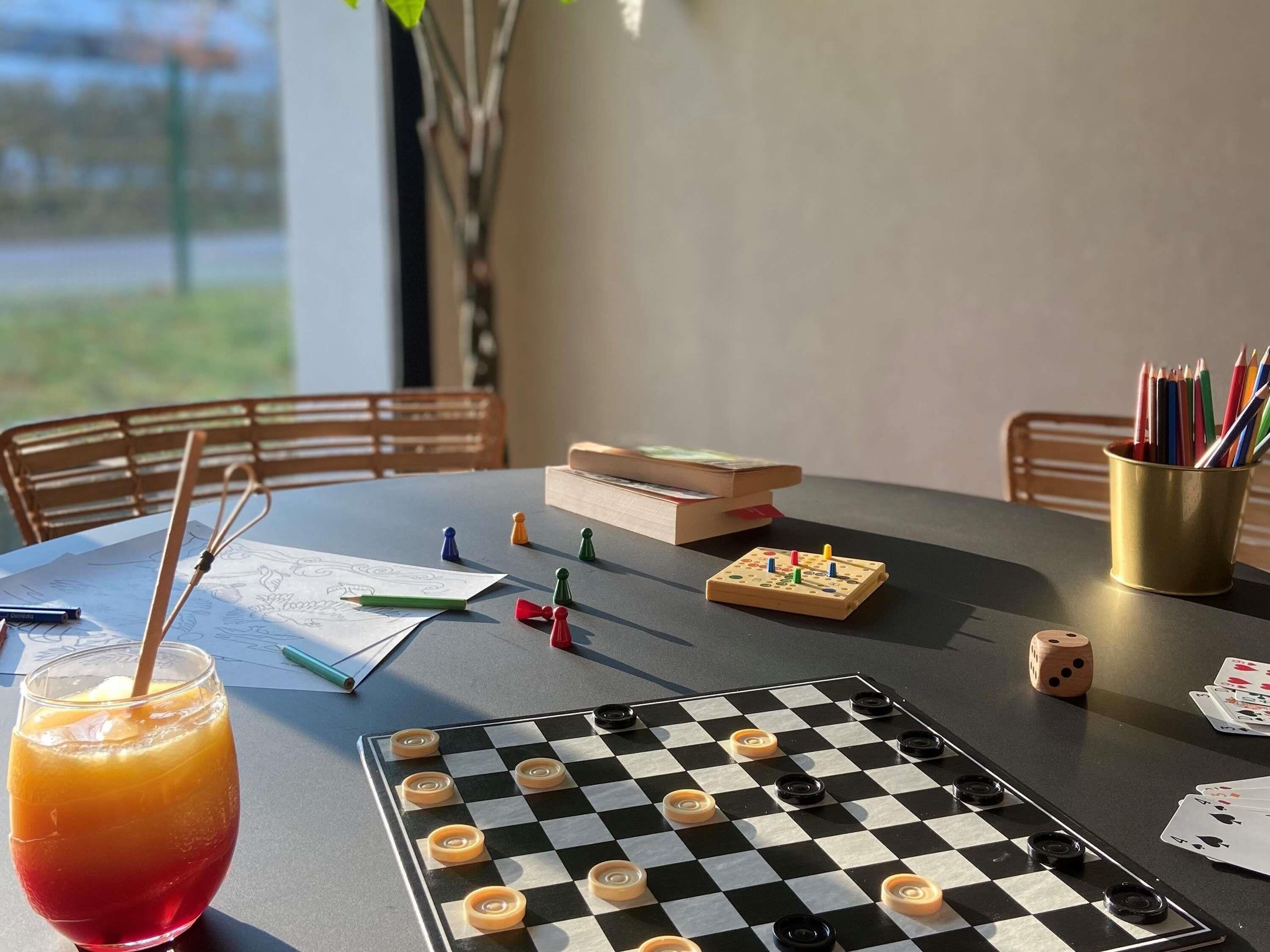 A table with a checkered board game, books, and a drink.