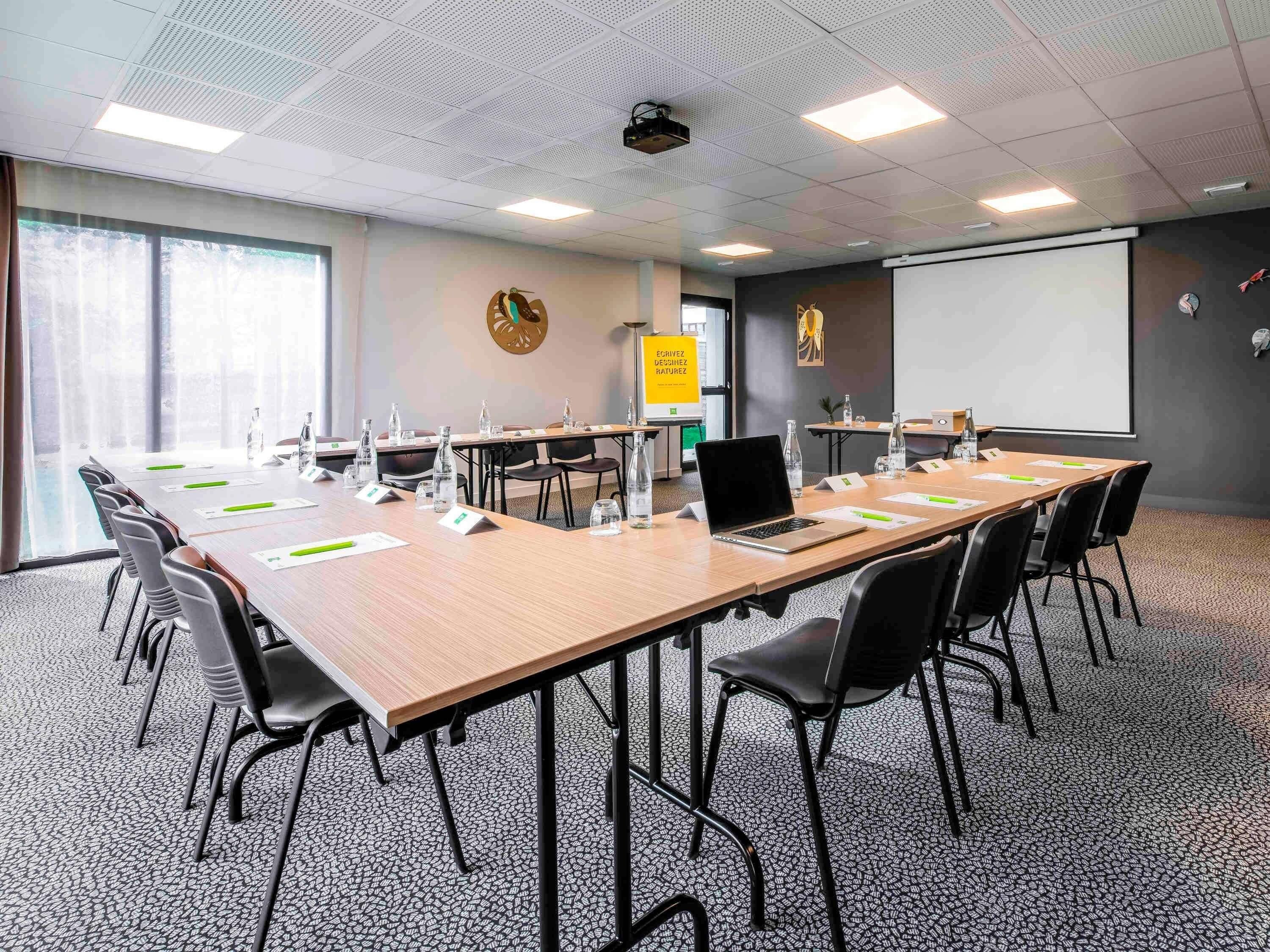 A conference room with a long table, chairs, a projector, a whiteboard, and a large window.