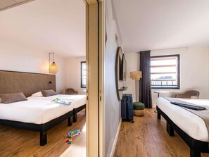 Une chambre d’hôtel avec deux lits, un grand miroir, une petite table et une fenêtre avec des rideaux.