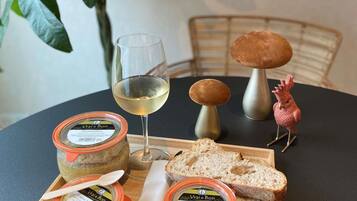 A table with a glass of white wine, two mushroom-shaped containers, a jar of cream, a slice of bread, and a decorative rooster.