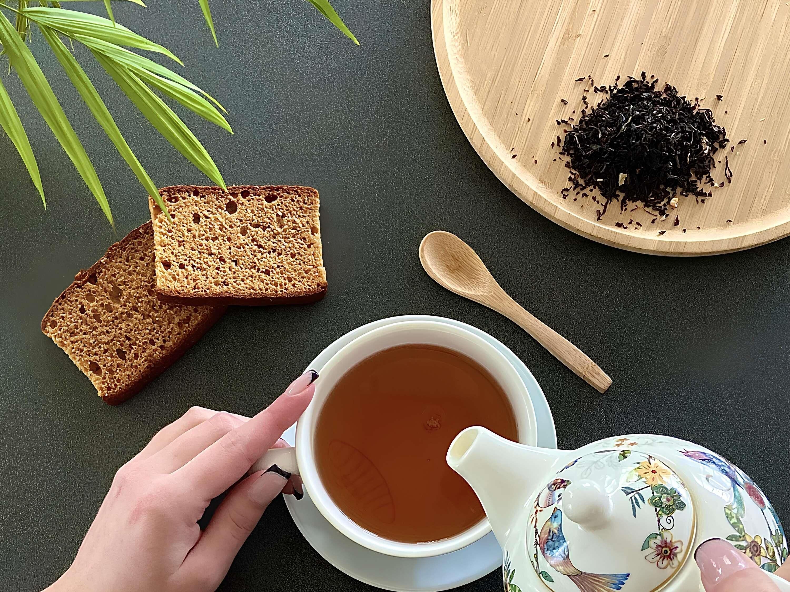 A cup of tea, a teapot, slices of bread, and a plate of tea leaves on a dark surface.