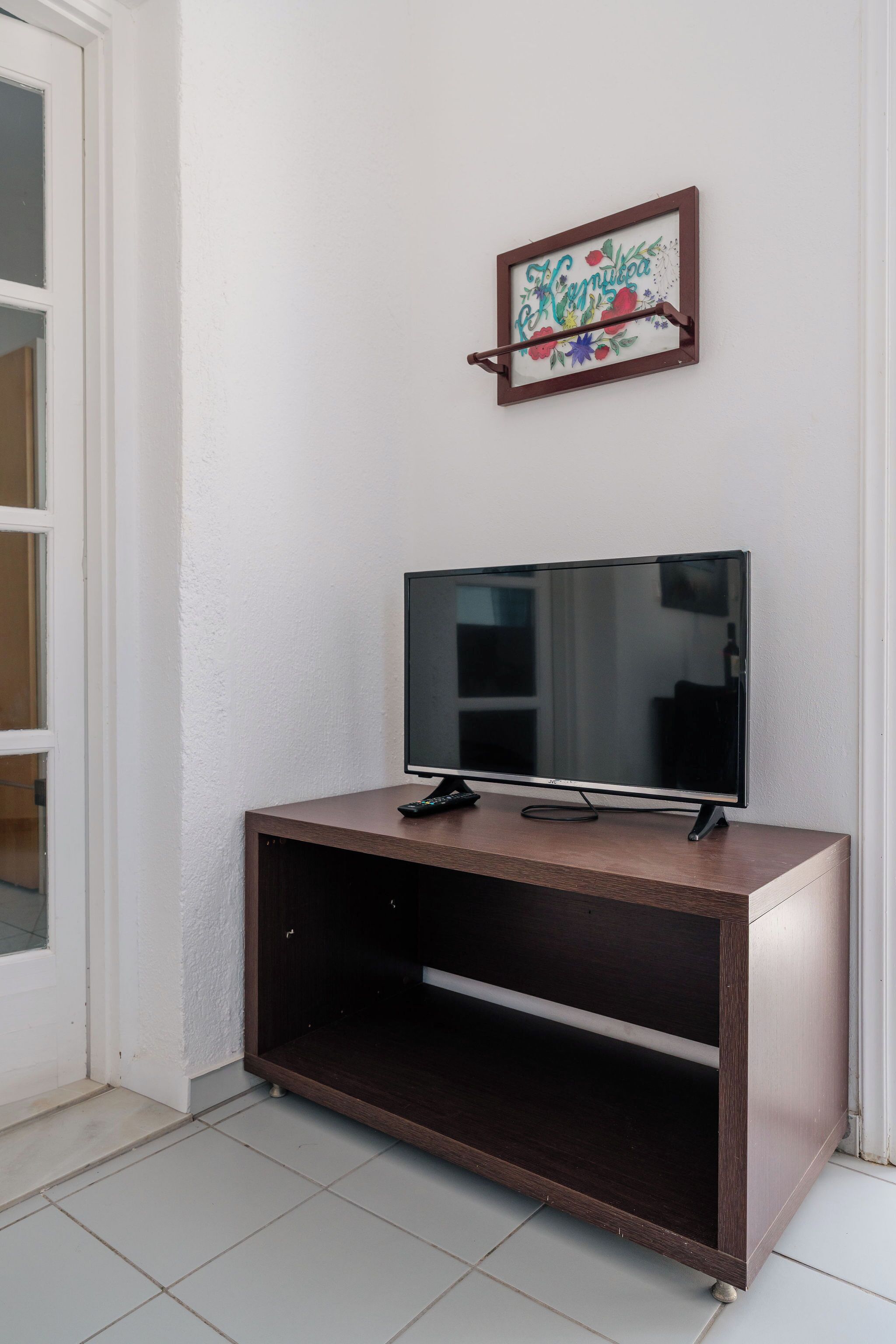 Un televisor sobre un soporte de madera, frente a una pared blanca, con un cartel enmarcado encima.