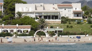Een gebouw aan de kust met een bord voor een restaurant, een strand ervoor en bergen op de achtergrond.