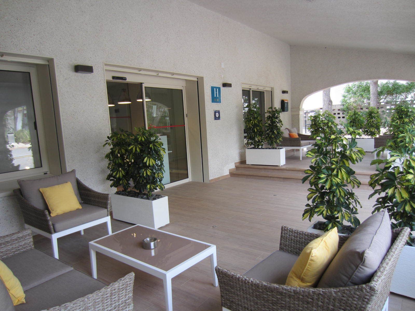 Un espacio al aire libre con mobiliario de mimbre, una mesa de centro y plantas en macetas.