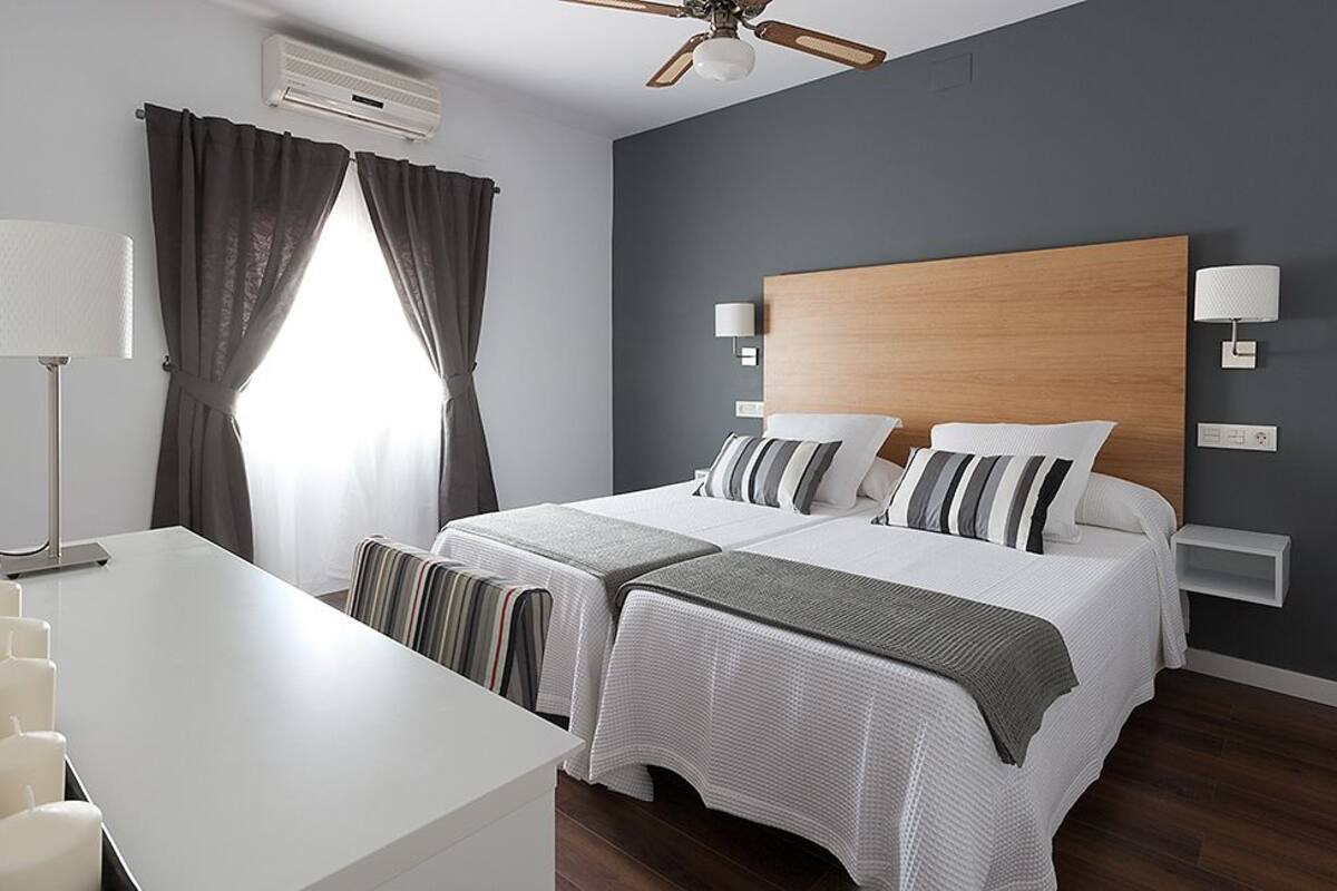 A modern hotel room with a large bed, two bedside tables, a desk, and a ceiling fan.