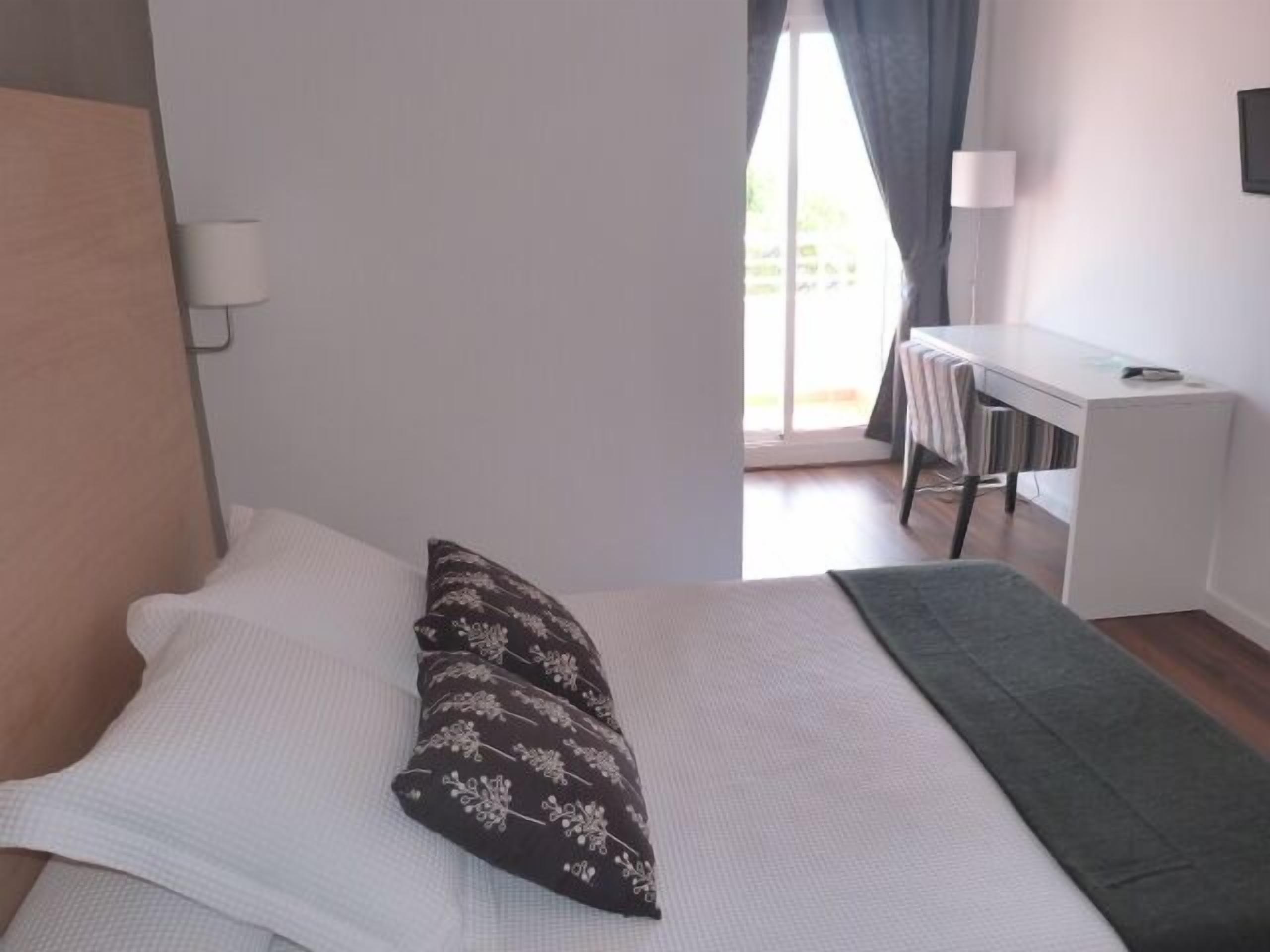 Un dormitorio con cama, escritorio y ventana con cortinas.
