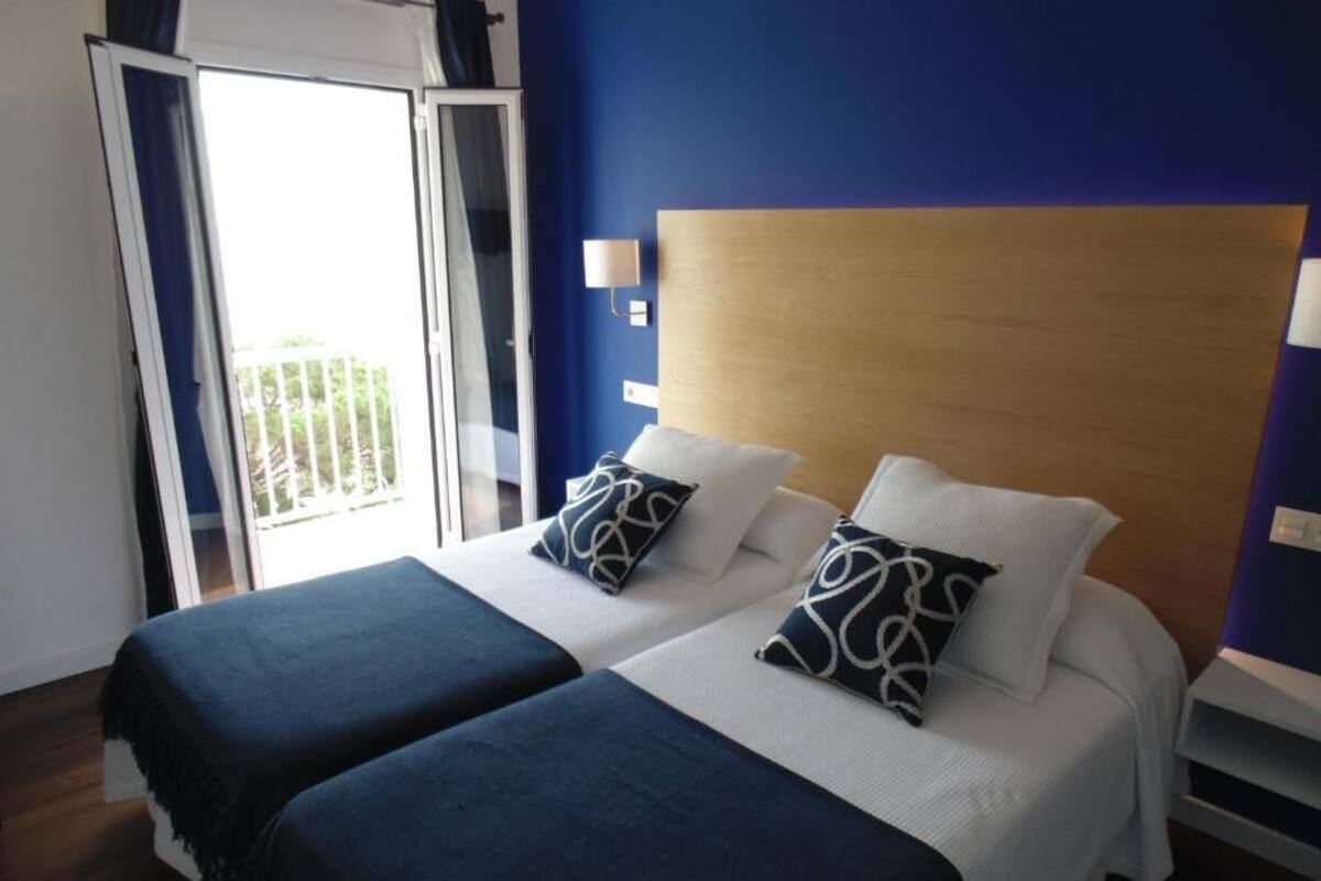 A double bed with a wooden headboard, two pillows, and a blue blanket.