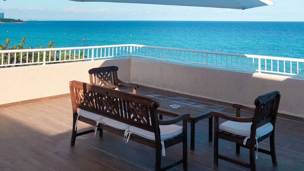 Een terras met een tafel en twee stoelen, met uitzicht op een heldere blauwe zee en een verre kustlijn.