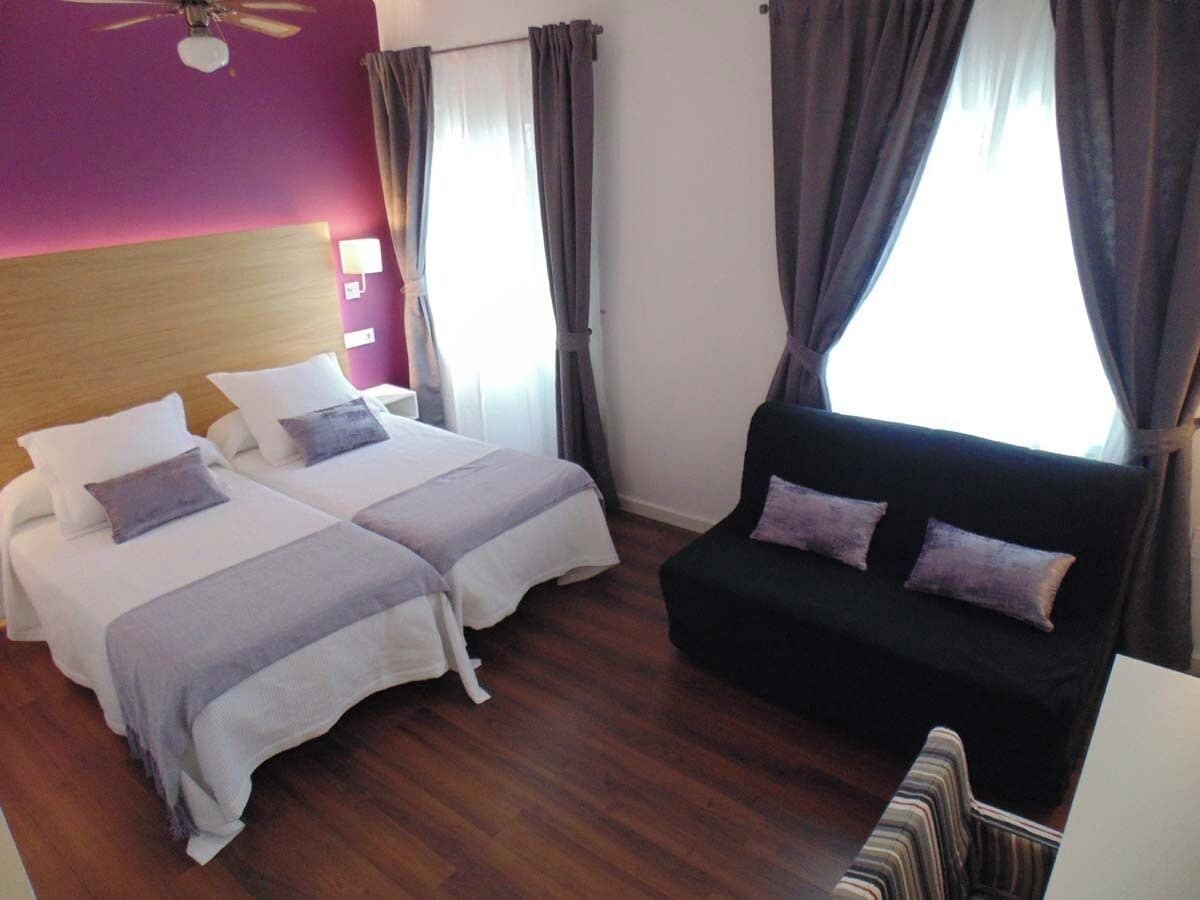 Une chambre d’hôtel avec deux lits, un canapé noir et un ventilateur de plafond.